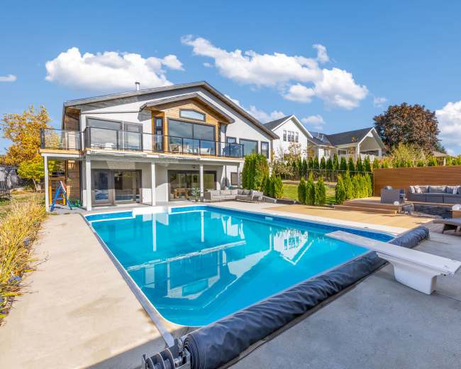 The image shows a modern two-story house with a swimming pool and outdoor seating area surrounded by greenery.