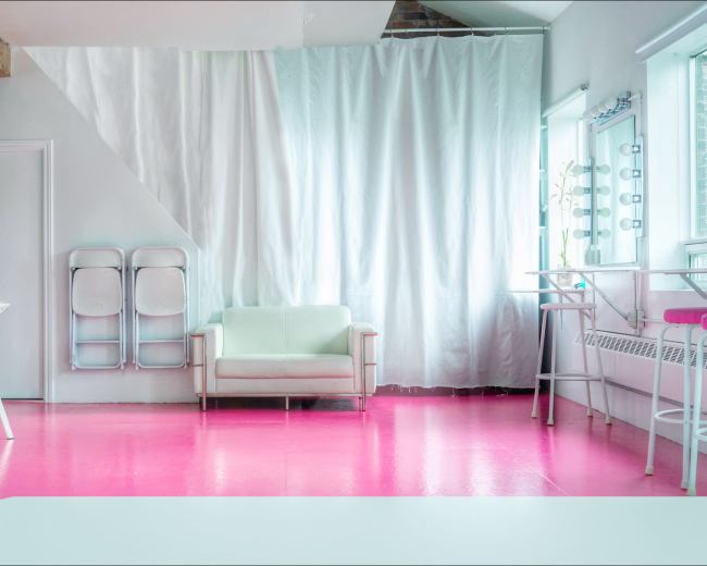 A modern room with pink flooring, a light green couch, and a bar area with stools.