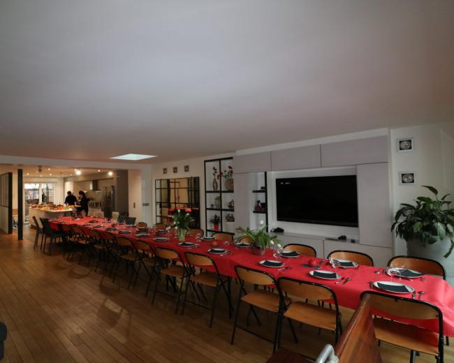 A large dining area features a long table set with red tablecloths and dinnerware, while the background shows a kitchen and seating area.