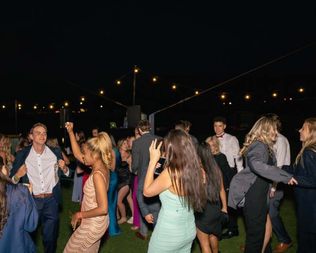 A group of people is dancing at an outdoor event under string lights at night.