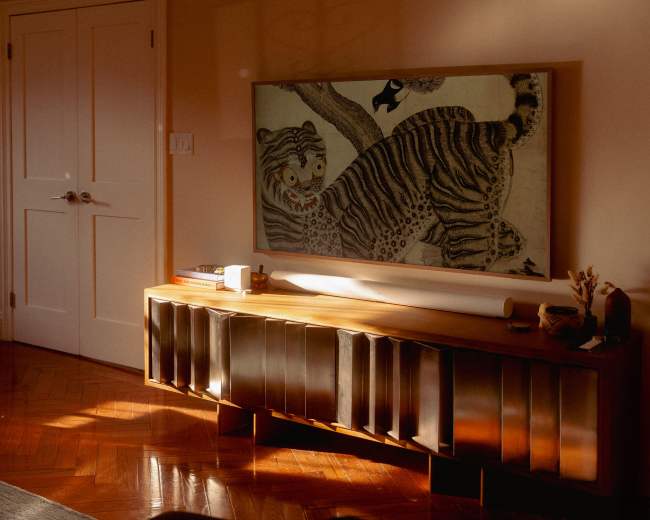A wooden sideboard with metallic accents displays a framed artwork of a tiger in a softly lit room.