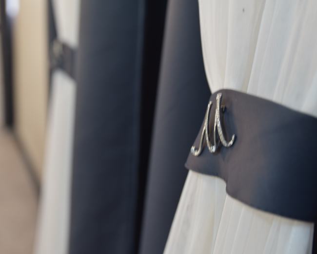 A close-up of a white curtain secured with a dark ribbon featuring a decorative clasp.