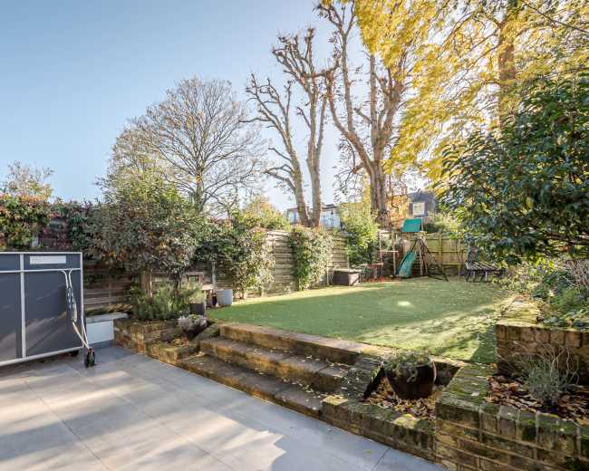 The image shows a backyard with a paved area, a lawn, and scattered trees and shrubs, along with a portable ping-pong table and a playground set in the background.