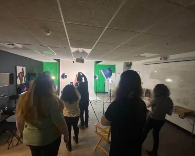 A group of people is standing in a studio with green screens and lighting equipment set up for a photoshoot.