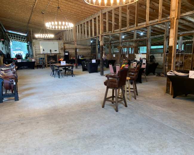 The image shows the interior of a barn with tables set up for an event, featuring black tablecloths and lighting fixtures hanging from the ceiling.