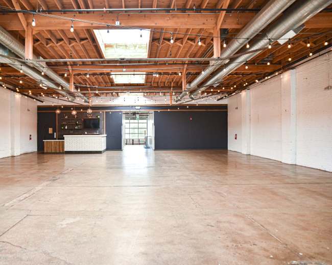 The image shows a spacious, vacant interior with polished concrete flooring, exposed wooden beams, and industrial-style lighting fixtures.