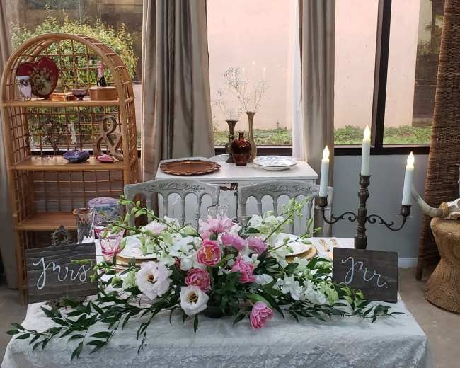 A decorated table set for a wedding, featuring floral arrangements, candle holders, and various decorative elements in a softly lit room.