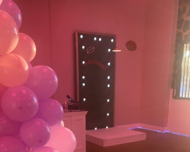 The scene features a playful interior decorated with clusters of purple balloons, a lighted backdrop, and a small stage area.