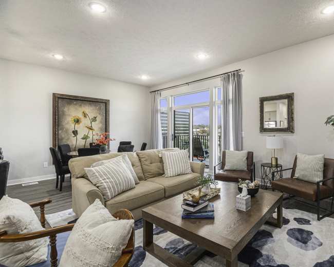 A modern living room features a beige sofa, a wooden coffee table, and large windows that open to a balcony view.