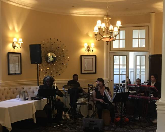 A small band performs in a well-lit room with elegant decor and seating arrangements.