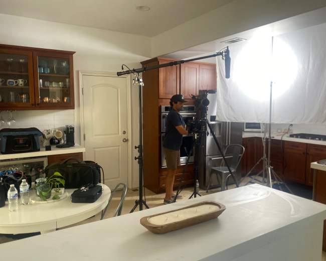 A person operates a camera setup in a kitchen equipped with wooden cabinets and professional lighting.