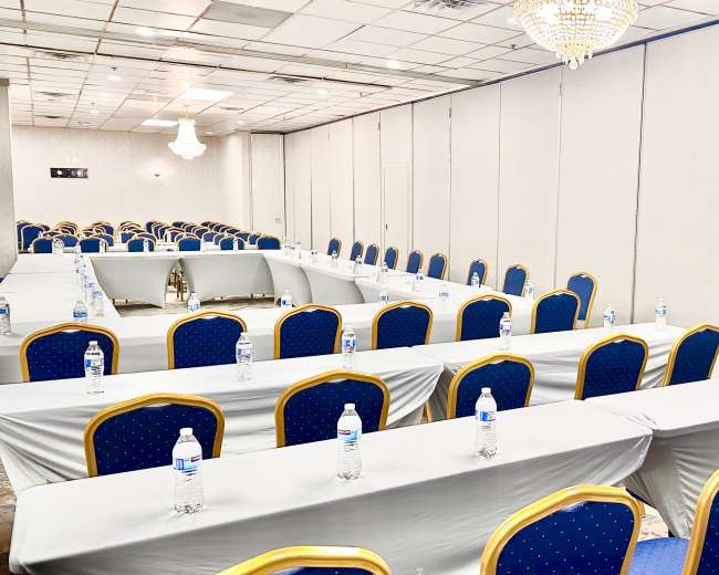 A conference room is set up with multiple rows of tables and blue chairs, each featuring a water bottle.