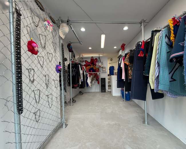A clothing store is depicted with a grid of hanging garments on both sides and a gated partition in the center.