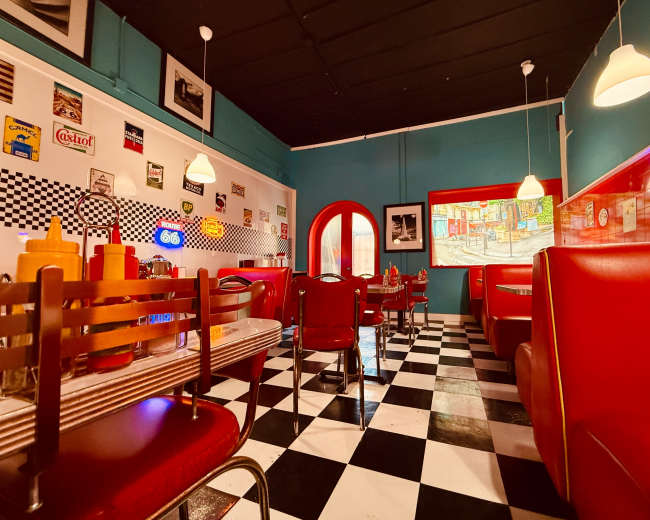 The image shows a brightly colored diner interior with red booths, black and white checkered flooring, and retro decor on the walls.