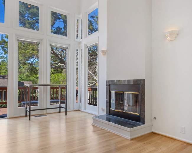 The room features large windows that provide natural light, a modern fireplace, and a wooden floor.
