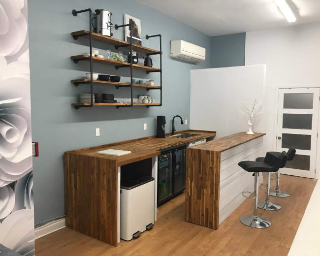 The image shows a modern kitchen with a wooden countertop, a small sink, and shelves displaying kitchen items, set against a blue wall.