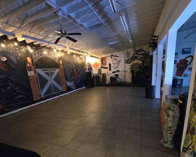 The image shows an empty, spacious room with murals on the walls and lights strung across the ceiling.