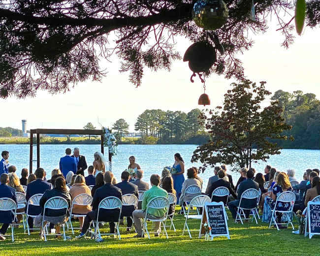 A wedding ceremony takes place by a lake, with chairs arranged in rows for guests and an altar set up near the water.