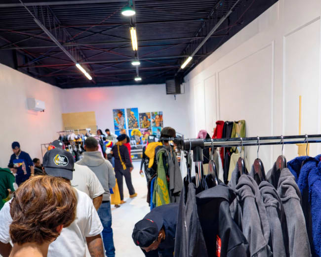 A clothing store features customers browsing racks of garments while others examine items laid out on a table.