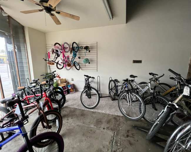 The image shows a bicycle shop with several bicycles parked on the floor and a wall displaying additional bikes and helmets.