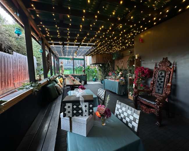 The image shows a decorated indoor space with festive lighting, dining tables covered in teal tablecloths, and various floral arrangements.