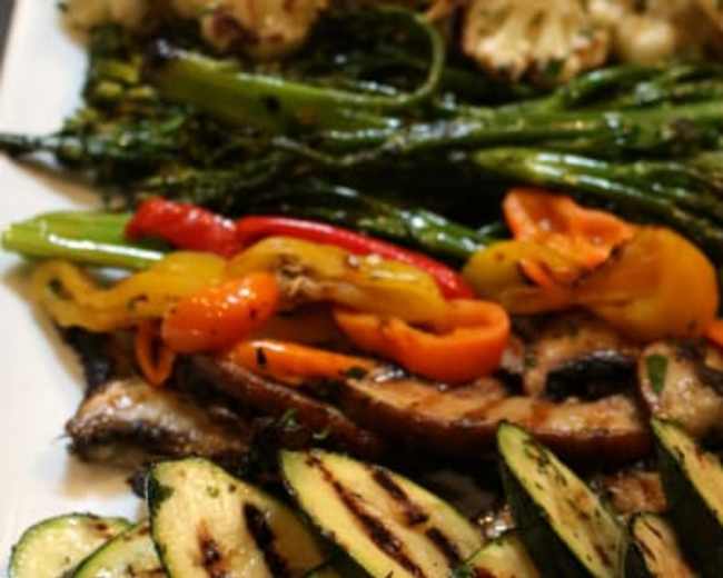 A platter of grilled vegetables, including zucchini, mini bell peppers, broccoli, and cauliflower, alongside grilled mushrooms.