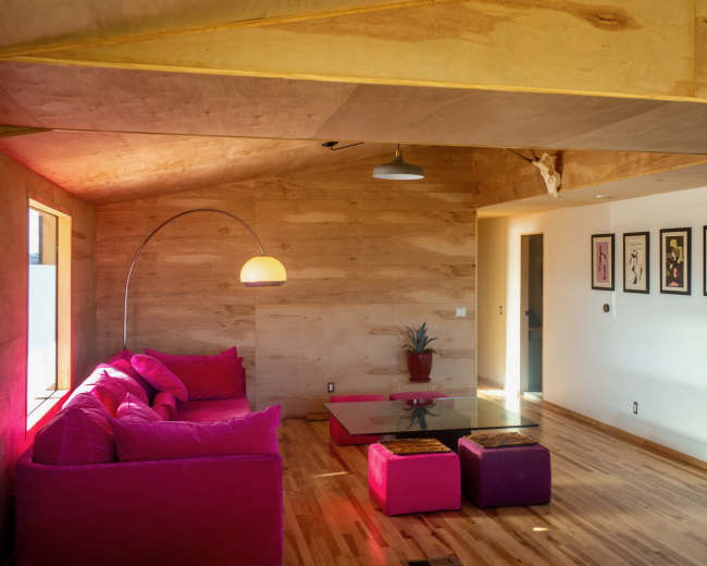 The image features a modern living room with wooden walls, a pink sofa, a glass coffee table, and decorative artwork on the walls.