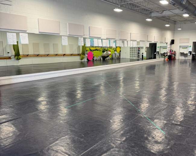 The image shows a large dance studio with a mirrored wall, black flooring, and some colorful decorations.