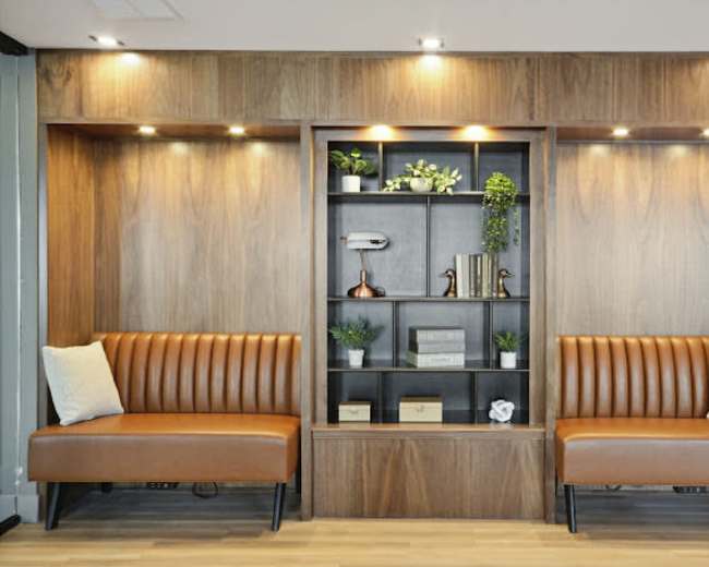 A modern interior features two brown leather benches flanking a wooden shelving unit with plants and decorative items.