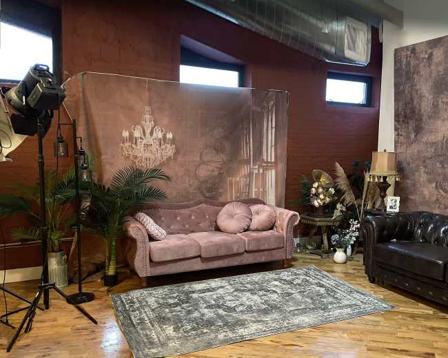 The image shows a photography studio with two sofas, a decorative backdrop, a rug, and various ornamental pieces.