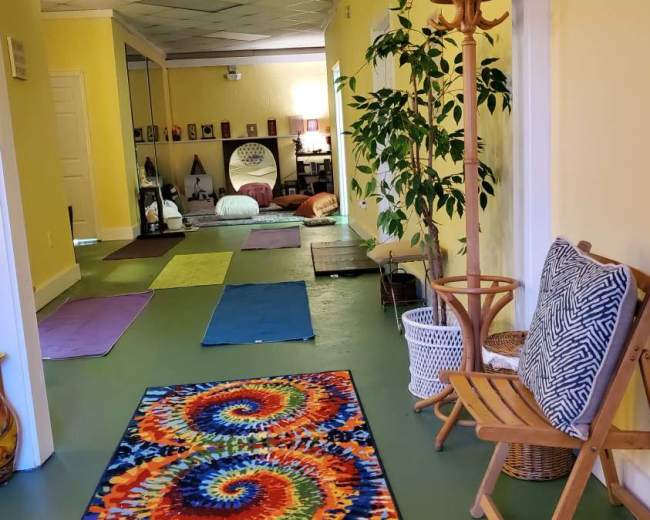 The image shows a brightly colored hallway leading into a room with yoga mats arranged on the floor and decorative elements like plants and furniture.