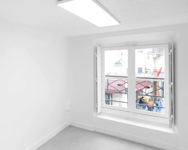 A bright, empty room with white walls and a large window overlooking an urban street.