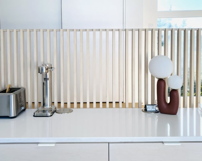A sleek kitchen countertop features a toaster, a beverage tap, and a decorative lamp behind a wooden slatted partition.