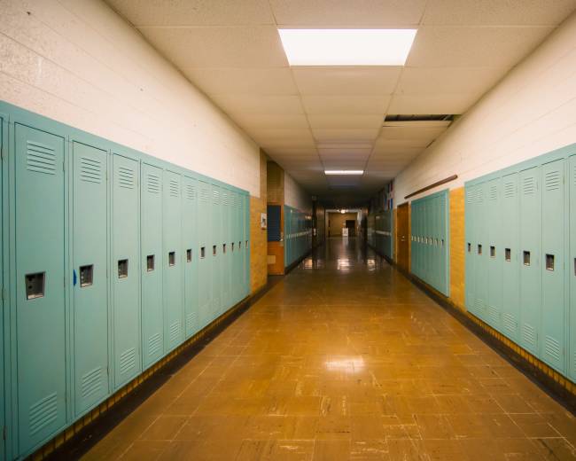 The image shows a narrow school hallway lined with turquoise lockers on both sides.