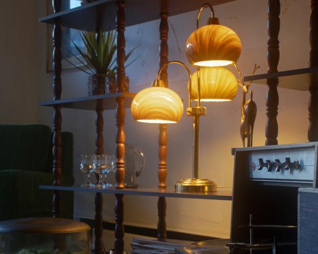 A cozy living room features a shelf with decorative items, glowing lamps, and a record player next to a vintage coffee table.
