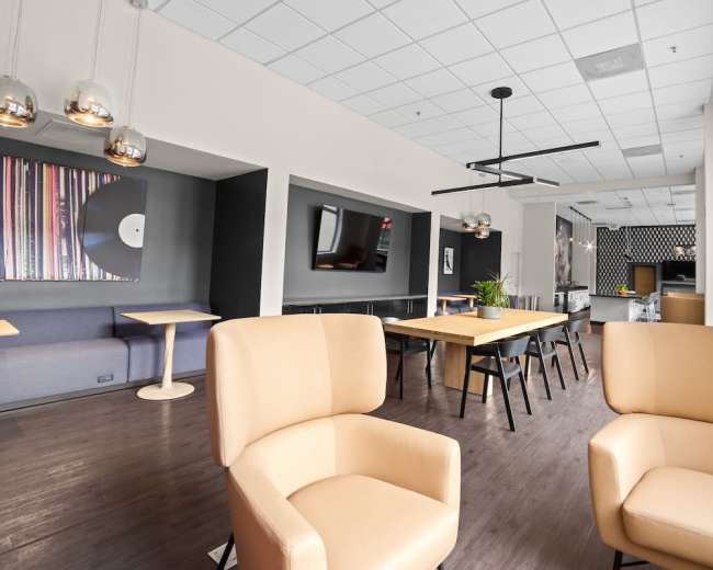 The image shows a modern, spacious lounge area with light-colored furniture, wooden floors, and decorative wall art.