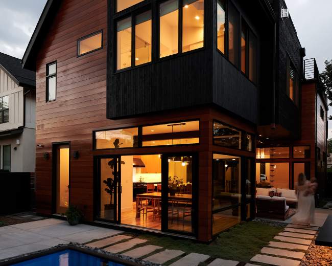 A modern two-story house with large windows overlooking a blue swimming pool and a pathway lined with stepping stones.