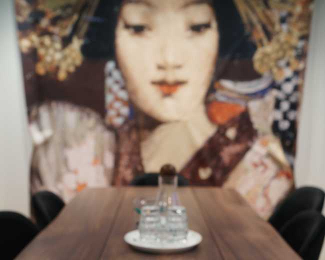 A large wooden table with a notepad and pen is positioned in front of a colorful wall art featuring a woman's face.