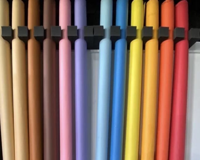 The image shows a row of rolled paper sheets in various colors, neatly arranged on a rack.
