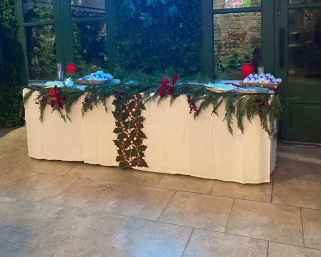 A table decorated with greenery and red accents is set up against a wall with a neon ghost sign above it.