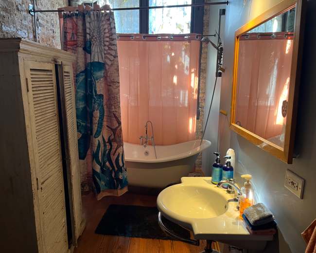 The bathroom features a freestanding bathtub, a pink shower curtain, a sink with toiletries, and a wooden cabinet against the wall.