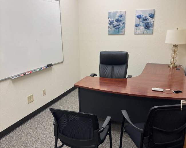 The image shows a tidy office with a desk, three chairs, a whiteboard, and two framed floral artworks on the wall.