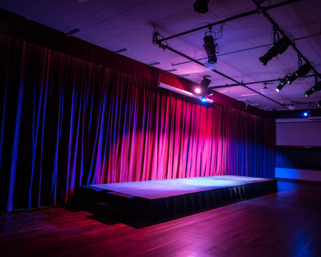 An empty stage with a raised platform and colorful curtains in a dimly lit room.
