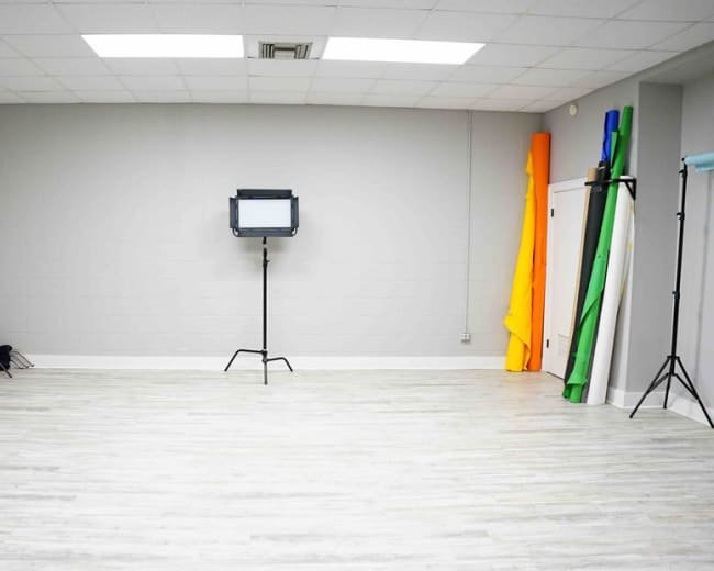 A spacious studio with gray walls, a light-colored floor, and various colored backdrops leaning against the wall.