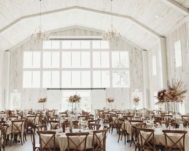 A spacious banquet hall with high ceilings, large windows, and neatly arranged tables adorned with floral centerpieces.