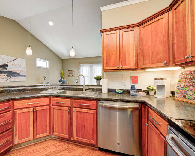A modern kitchen features wooden cabinetry, a stainless steel dishwasher, and a countertop with various kitchen appliances and utensils.