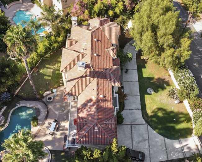 The image shows an aerial view of a large residential property featuring a swimming pool, landscaped garden, and a driveway.