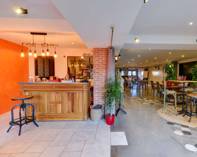 The image shows a modern interior space featuring a wooden bar area with a vibrant orange wall, leading into a dining area with varied seating arrangements and decorative plants.