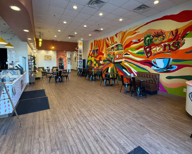 The image shows a vibrant café interior featuring colorful wall murals, wooden flooring, and tables arranged for dining.