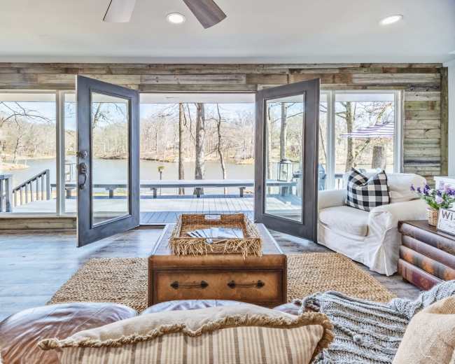 A cozy living room with large open doors leading to a deck overlooking a lake.